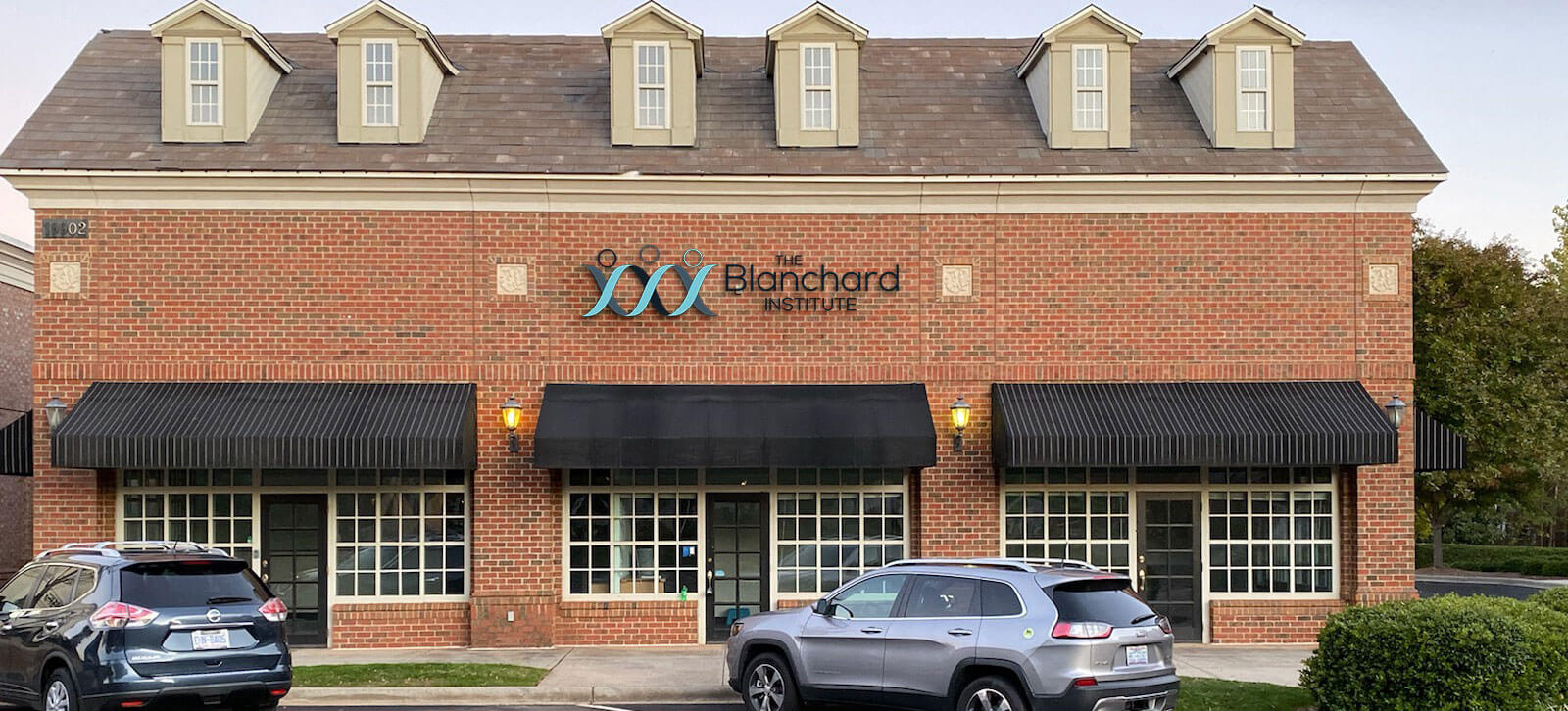 A brick building with three black doors and three awnings with a sign that reads The Blanchard Institute centered in the middle.