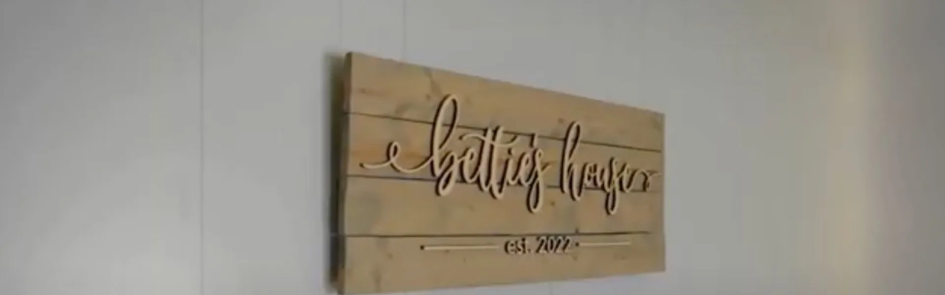Wooden wall sign with cursive text that reads "Bettie's House," mounted on a white wall.