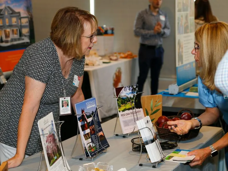 Two businesswomen having a conversation and reviewing mental health and recovery resources at Recovery Awareness Day.