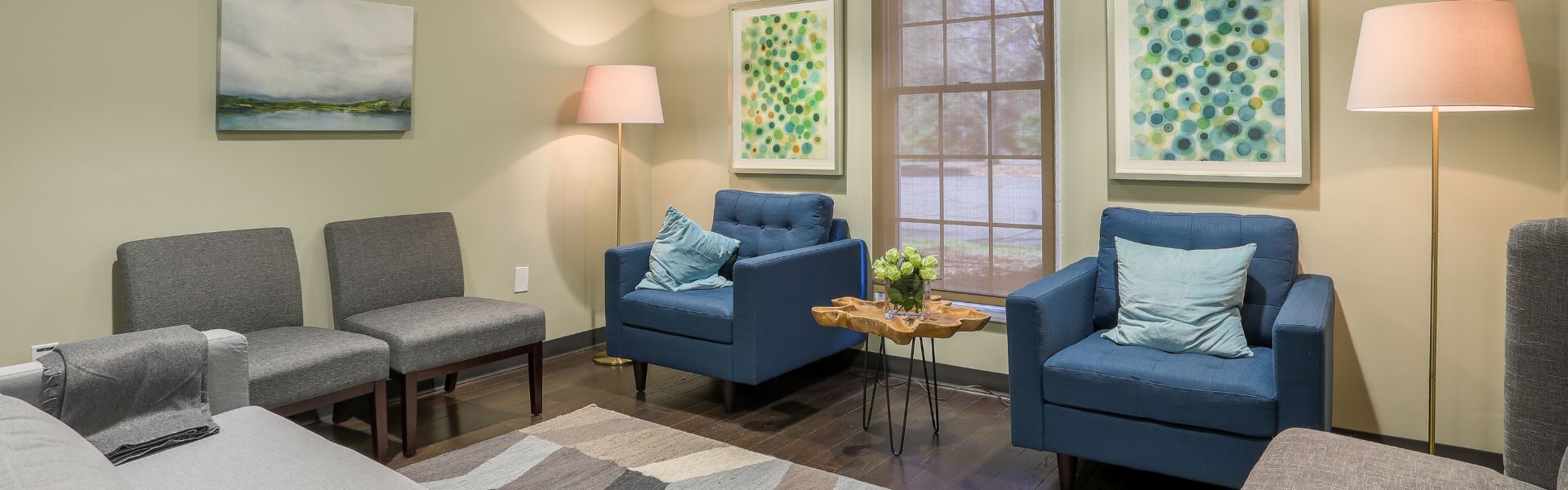 Comfortable therapy room with blue armchairs, gray guest chairs, soft lighting, and calming artwork, designed to create a warm and welcoming environment for mental health treatment in Charlotte, NC.