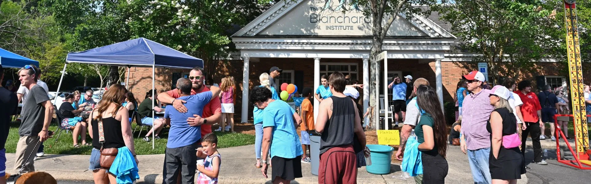 Outdoor community celebration event with balloons at The Blanchard Institute with families, staff, and visitors smiling and having a good time playing carnival games outside the treatment building.